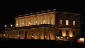 Un edificio grande e iluminado, con una fachada simétrica, múltiples ventanas en arco y una entrada central.