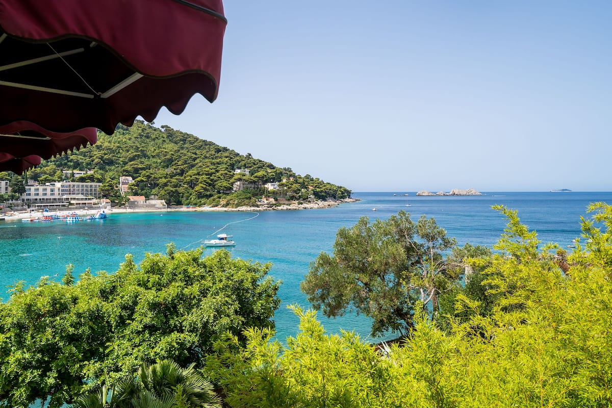 A coastal view with a boat docked near a building, surrounded by lush greenery and clear blue waters.