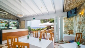 A restaurant with a stone wall, a bar with bottles, and tables with chairs.