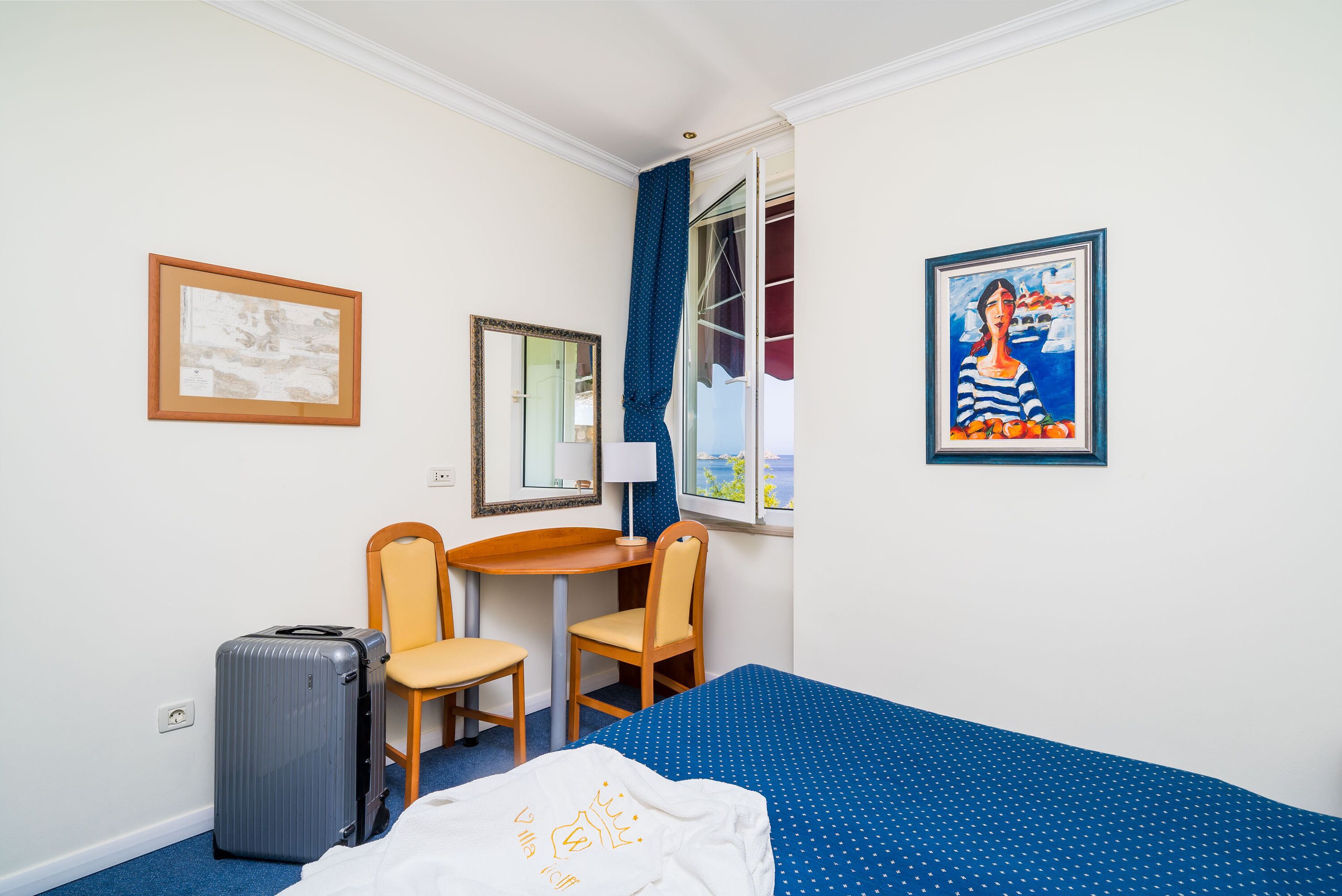A hotel room with a bed, a desk, two chairs, a suitcase, and a window with curtains.