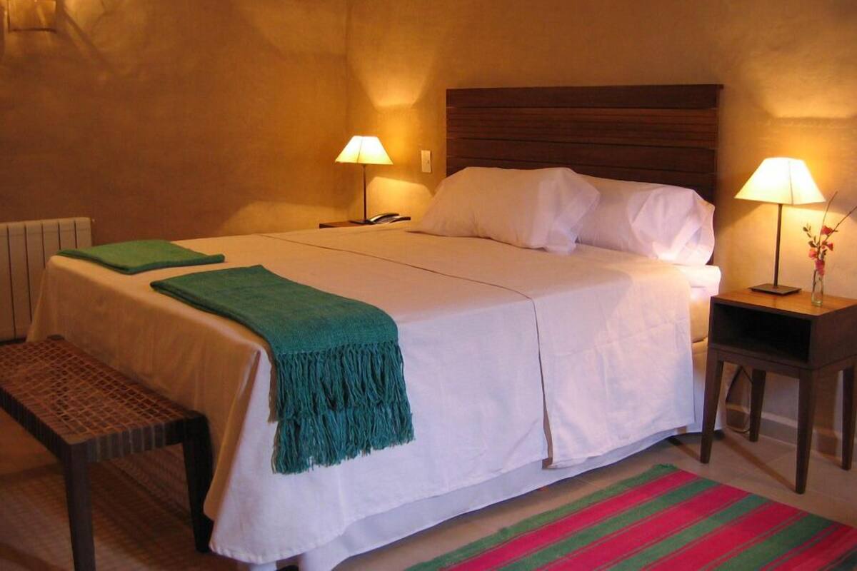 A hotel room with a large bed, two bedside tables, a bench, and a colorful striped rug.