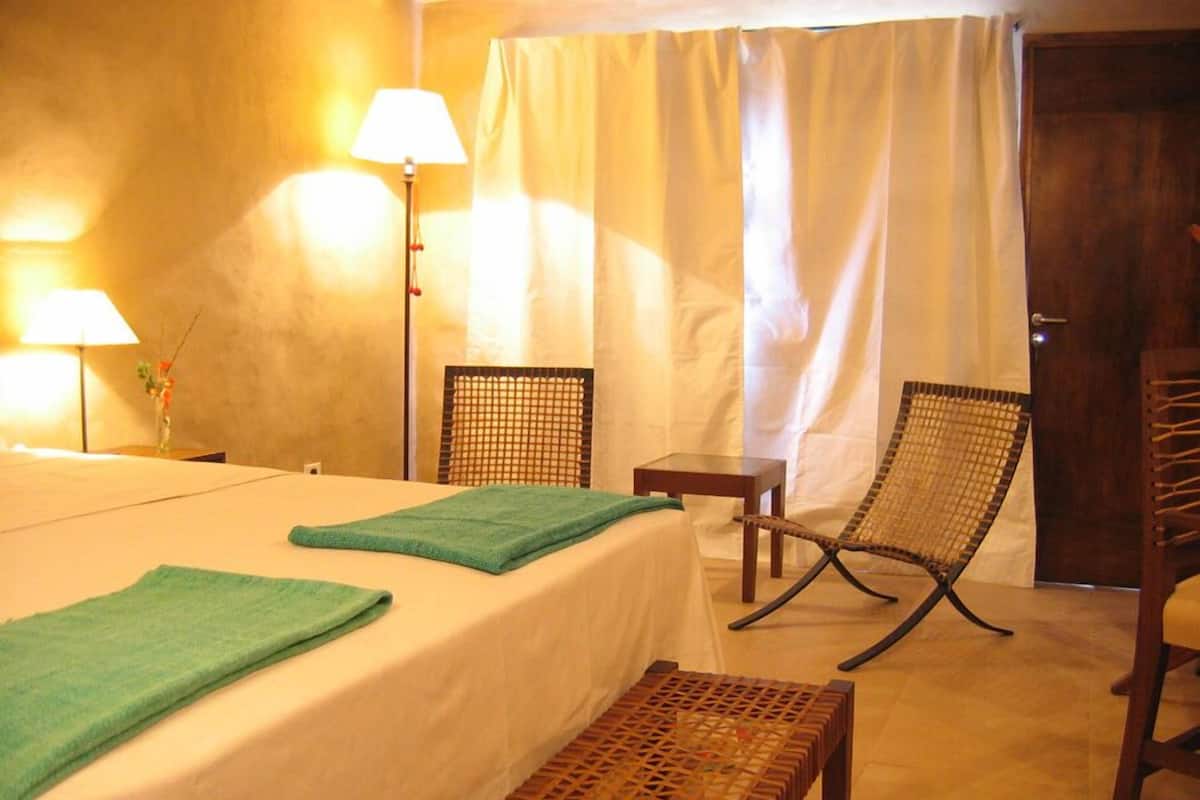 A hotel room with a bed, two chairs, a small table, and a lamp.