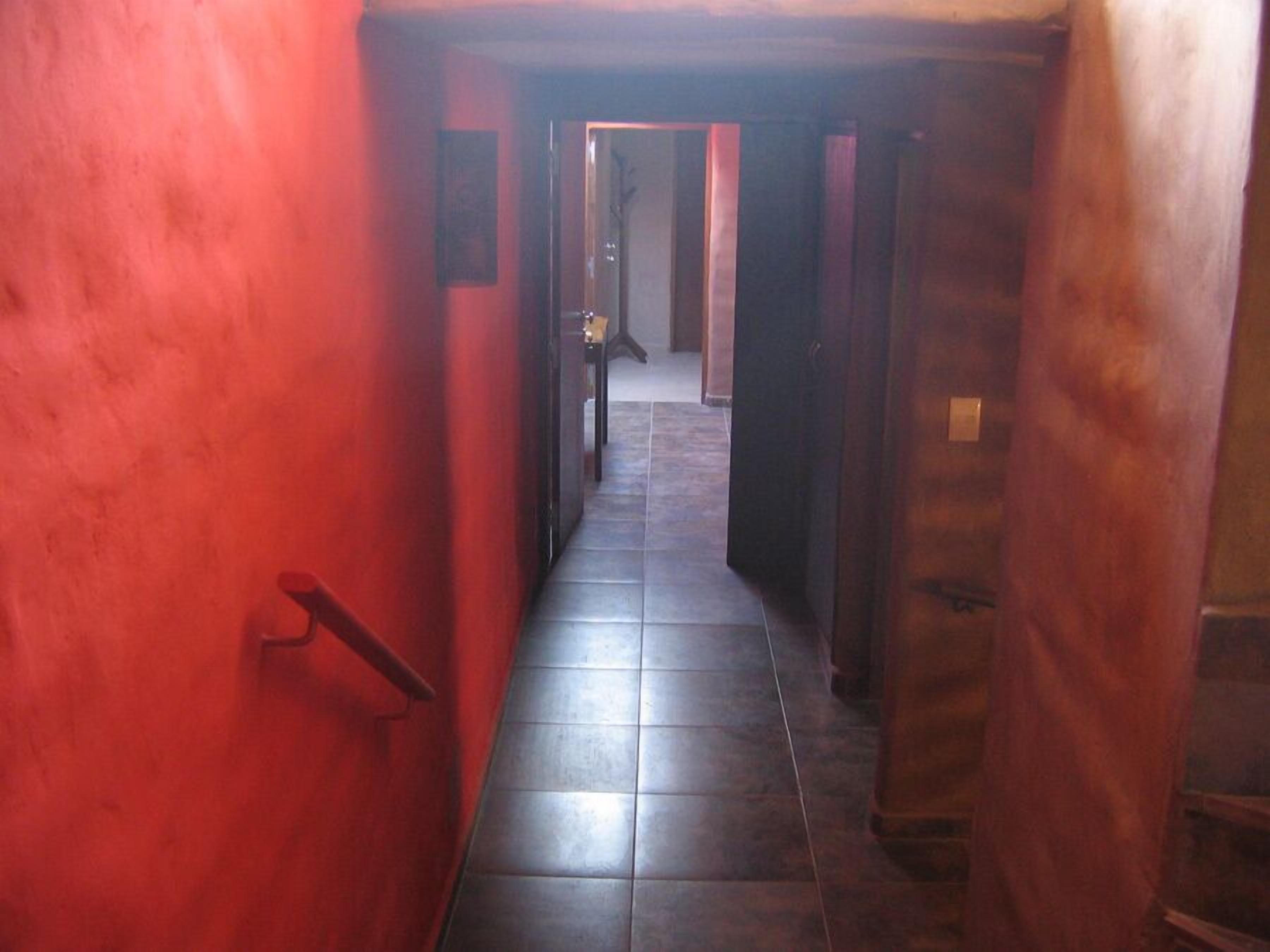 Un pasillo estrecho con una pared roja y piso de baldosas, que conduce a una puerta al final.