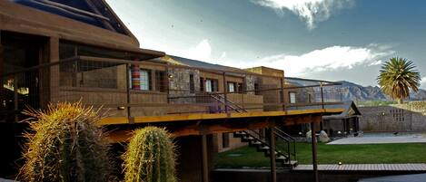 A modern building with a glass facade, a wooden deck, and a staircase leading to a pool area.