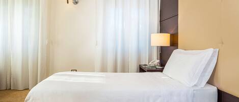 A hotel room with a large bed, a bedside table with a lamp, and a phone.