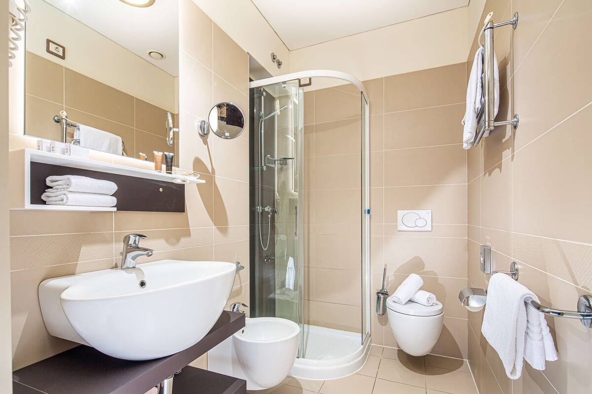 A modern bathroom with a large white sink, a glass-enclosed shower, and a toilet with a towel rack.