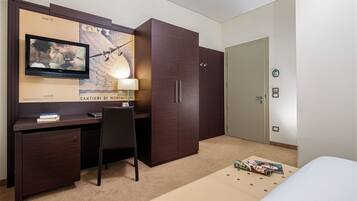 Een hotelkamer met een bed, een bureau met stoel, een kledingkast, een aan de muur bevestigde televisie en een lamp.