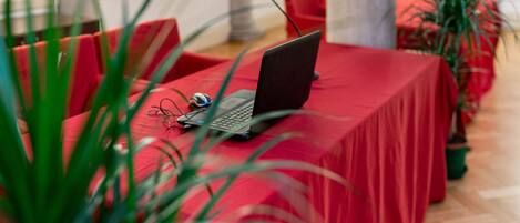 Una habitación con una mesa roja, una computadora portátil y un micrófono. Hay sillas rojas y plantas en macetas.