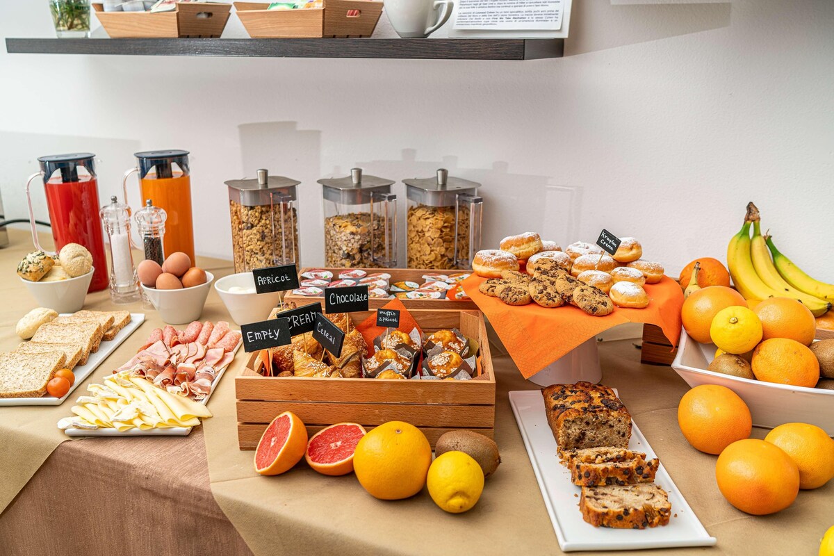 Un bufé con diversas opciones de comida, incluyendo pan, pastelería, frutas y bebidas.