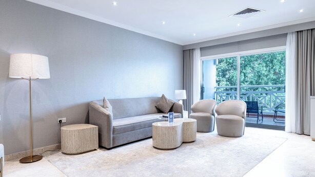 A modern living room with a sofa, two round side tables, a floor lamp, and a view of a balcony. - Argan Al Bidaa Hotel and Resort (Salmiya)