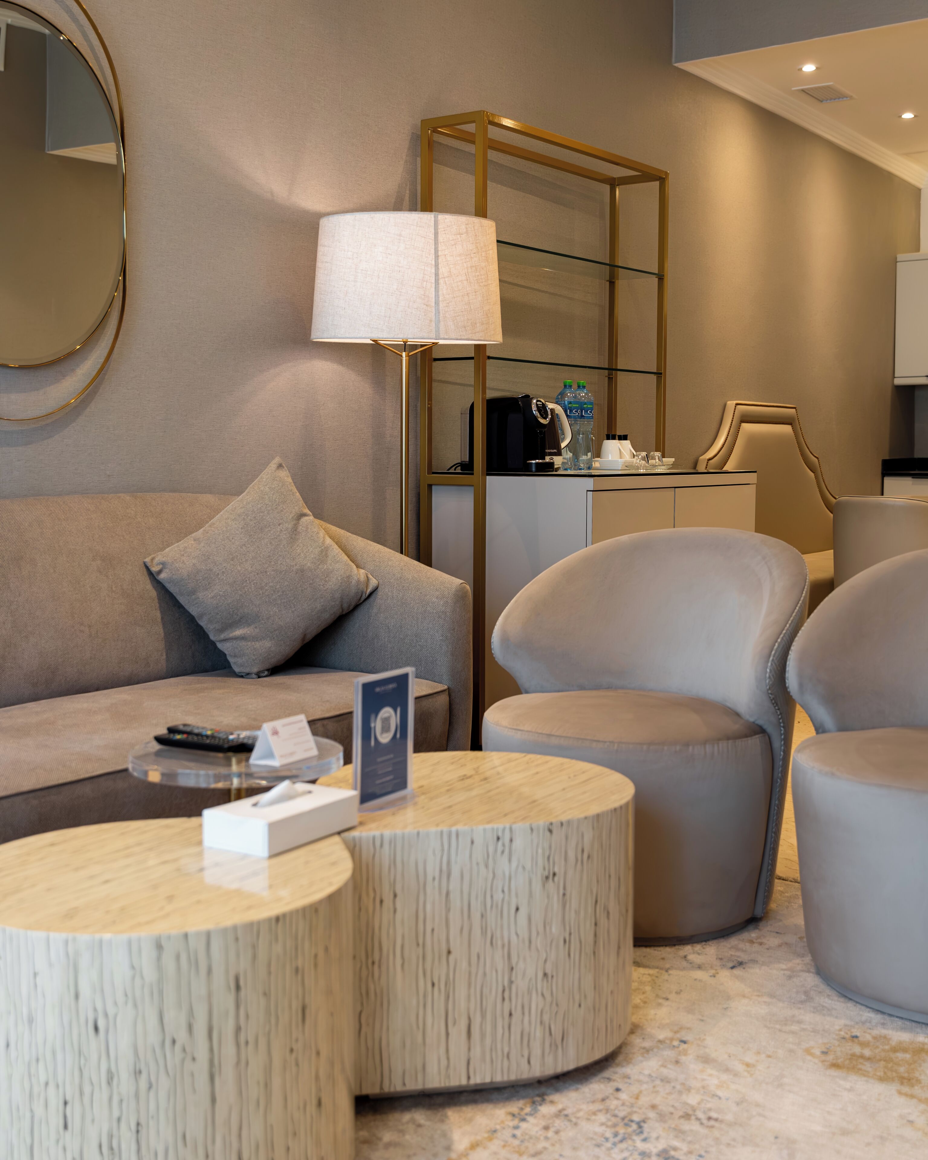 A modern living room with a sofa, two armchairs, a coffee table, a lamp, and a side table with a mirror and decorative items.