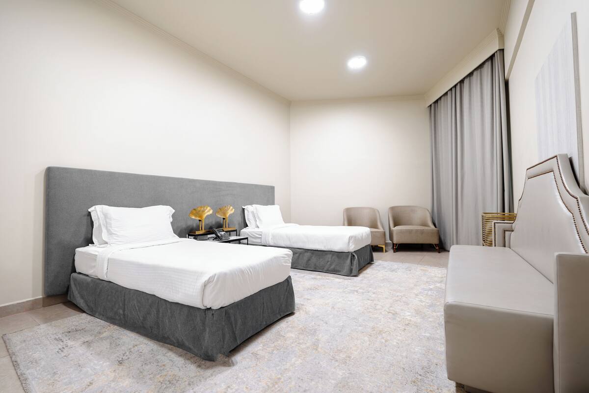 Een hotelkamer met twee bedden, een bank, een stoel en een groot raam met gordijnen.