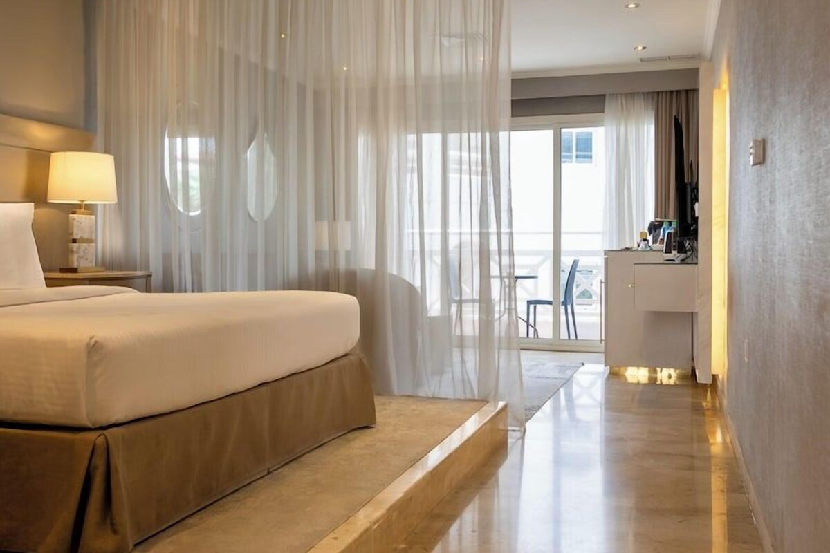A modern hotel room with a large bed, a desk, and a view of the city.