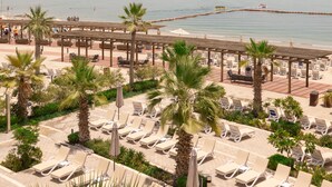 A beachside resort with sun loungers, palm trees, and a view of the sea. - Argan Al Bidaa Hotel and Resort (Salmiya)