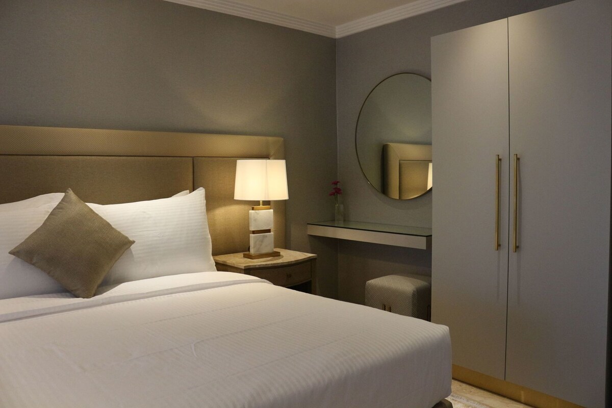 A hotel room with a bed, a nightstand with a lamp, a mirror, and a wardrobe.