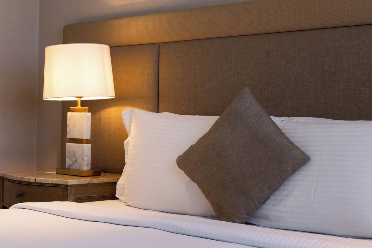 Een net opgemaakt bed met witte lakens, een bruin hoofdbord en een bedlamp met een marmeren voet.