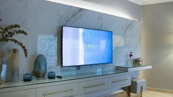 A modern living room with a flat-screen TV on a glass console, marble wall, and minimalist decor.