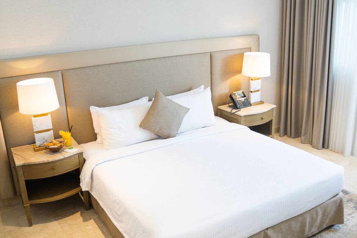 Een hotelkamer met een groot bed, twee nachtkastjes met lampen, een telefoon en een paar slippers op de vloer.