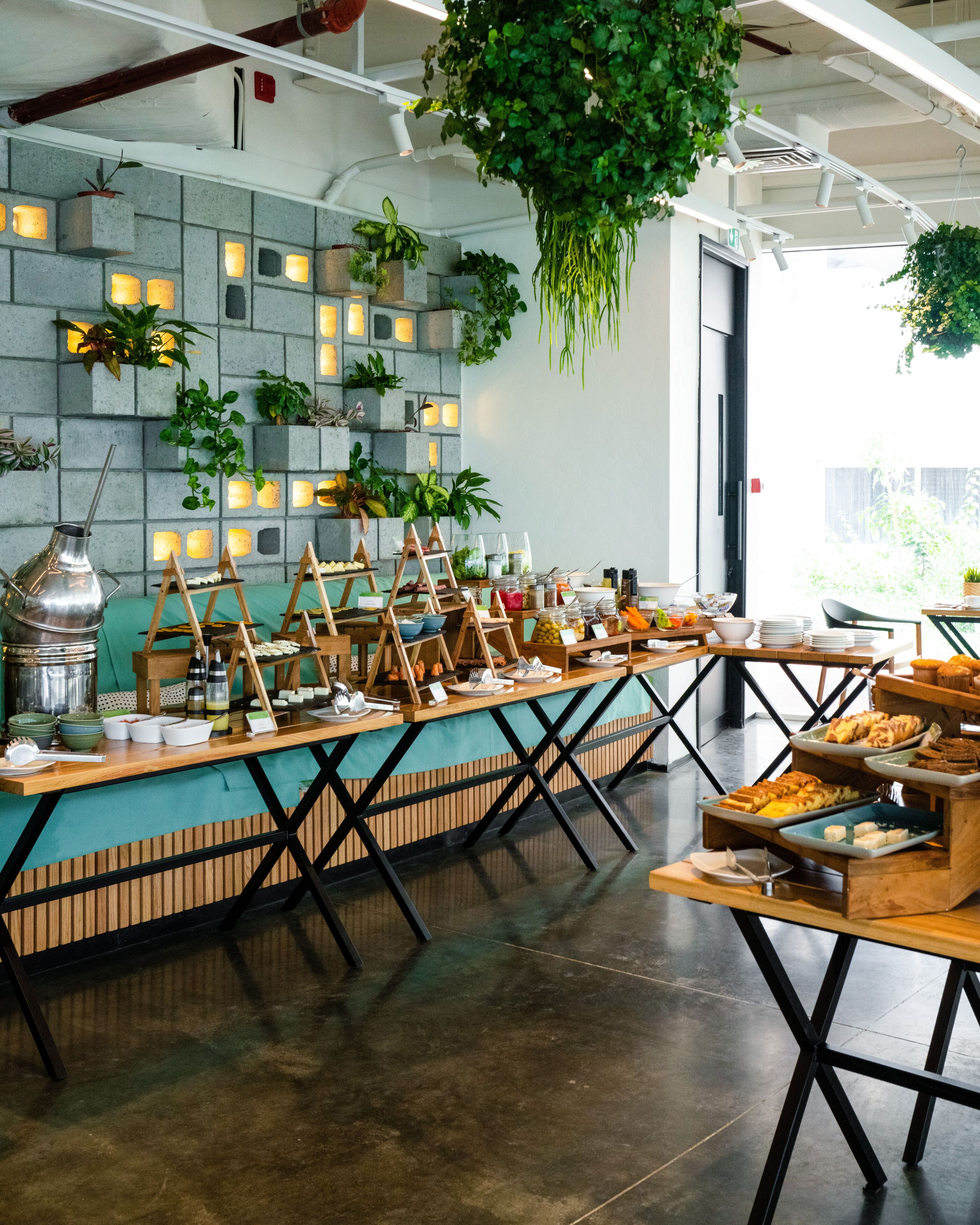 Un espace repas moderne avec une longue table conviviale, des chaises en bois et une variété d’aliments présentés sur des présentoirs à plusieurs niveaux.