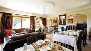 A dining area with a long table set for a meal, a sofa with cushions, and a window with curtains.
