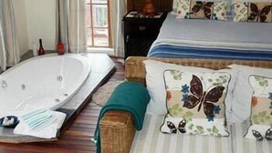 A bedroom with a large bed, a wooden headboard, a nightstand, a lamp, and a bathtub.