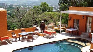 A pool area with a curved edge, outdoor furniture, and a view of the city in the background.