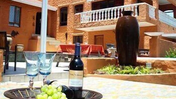 A building with a textured facade, a balcony, and a table with a bottle and glasses.
