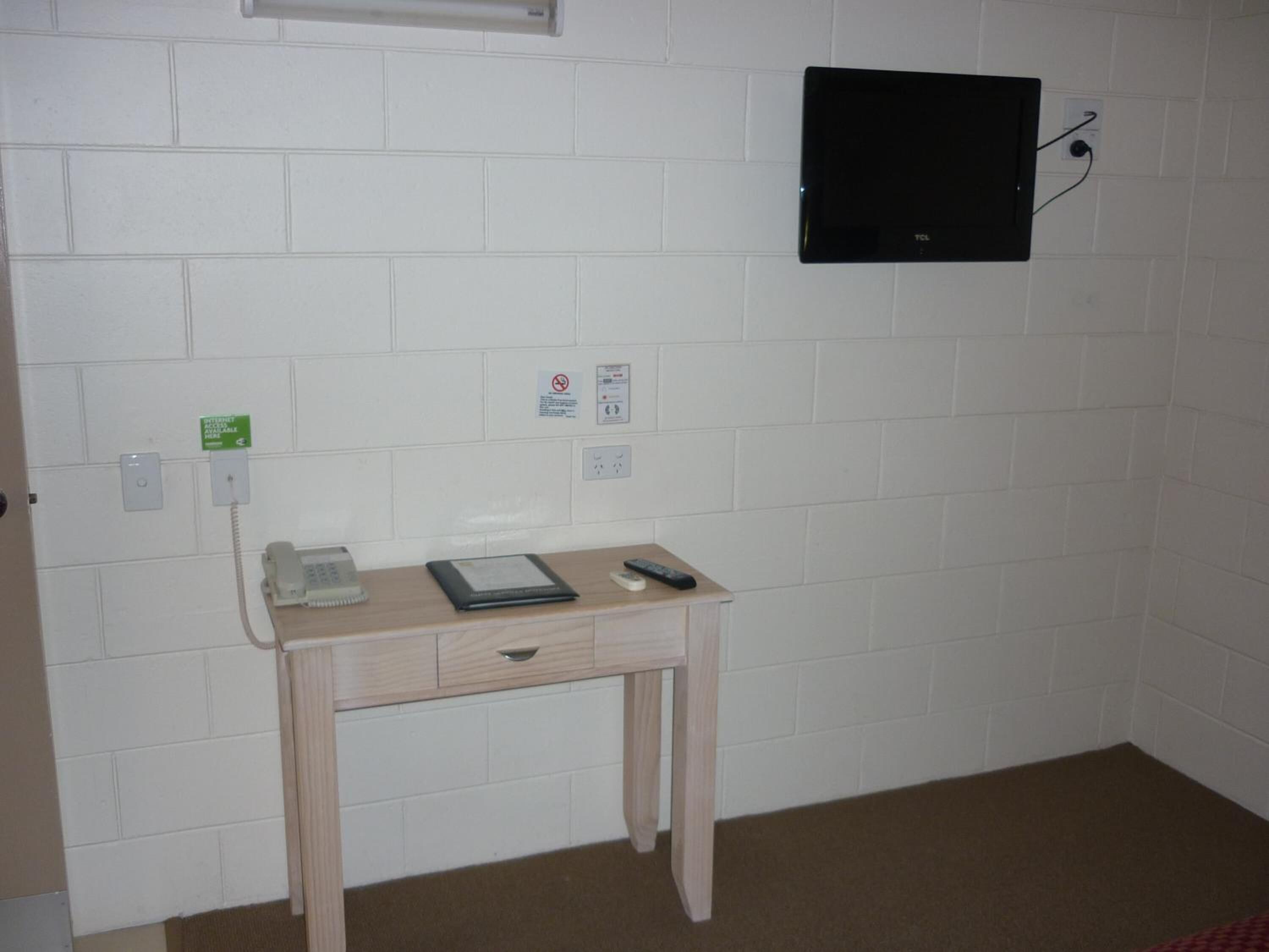 A small room with a wooden desk, a telephone, a black panel, and a wall socket.