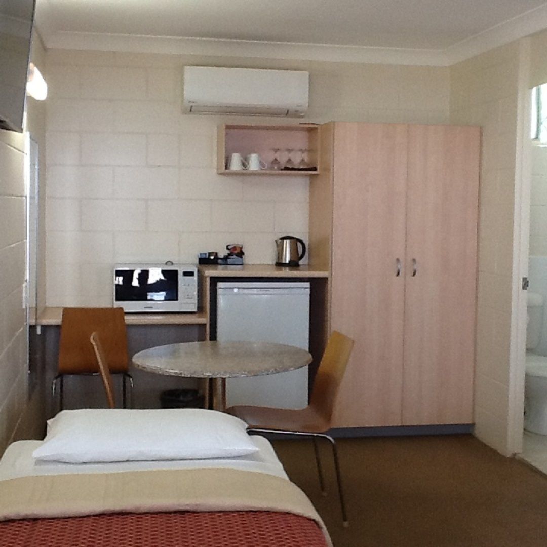 A compact hotel room with a single bed, a small kitchenette, a television, and a wardrobe.