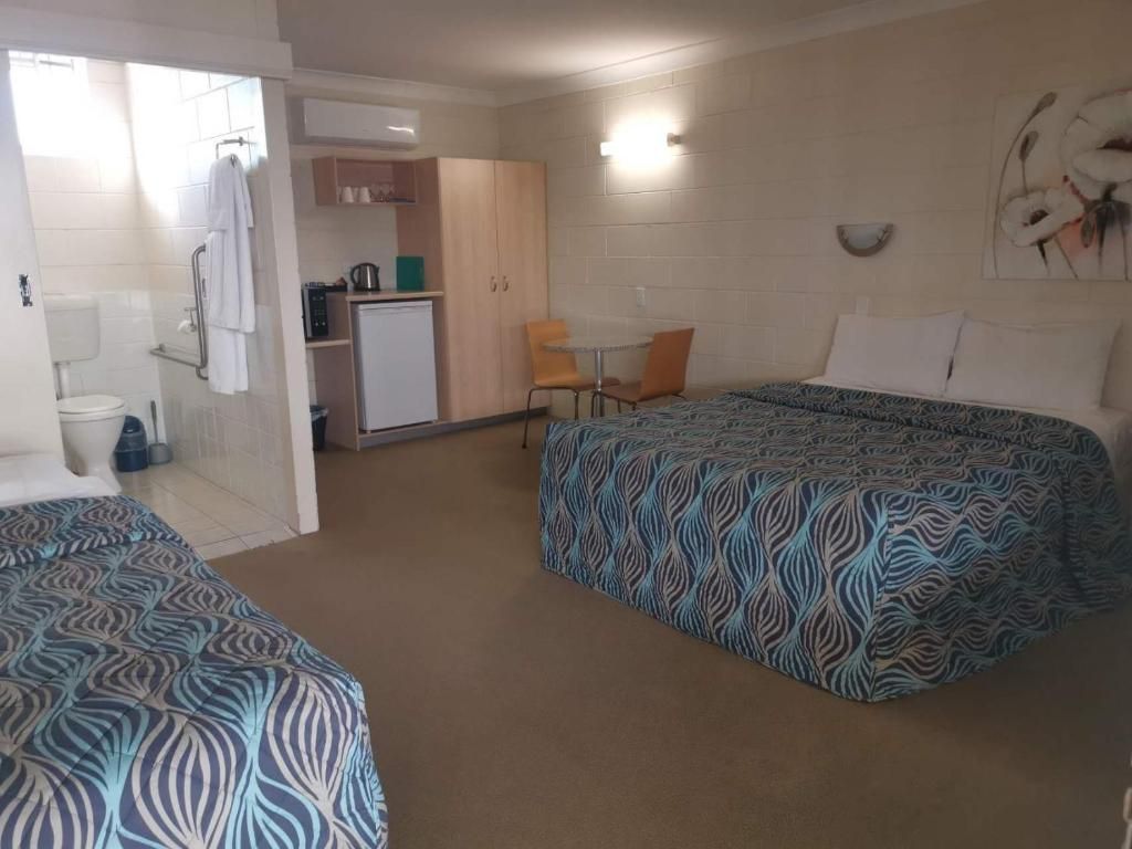 Une chambre d’hôtel avec deux lits, une kitchenette, une petite table à manger et un espace douche.