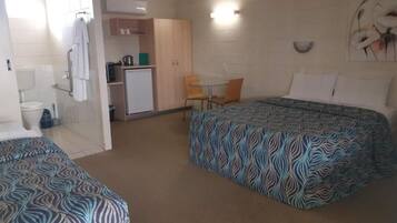 Une chambre d’hôtel avec deux lits, une kitchenette, une petite table à manger et un espace douche.