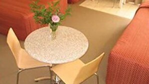 A small round table with a vase of flowers, two chairs, and a red couch.