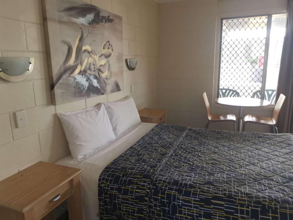 A hotel room with a bed, a nightstand, a painting on the wall, a window with a view, and a table with chairs.