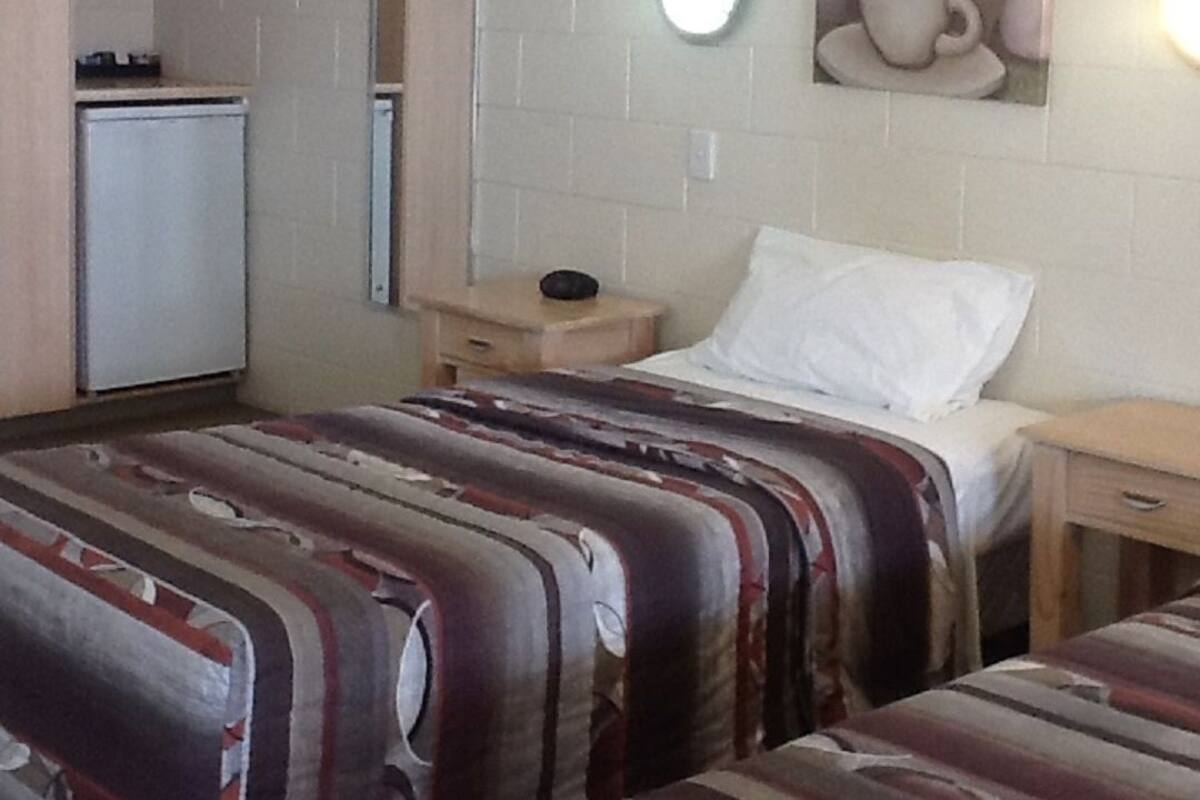 Habitación de hotel con dos camas, una kitchenette pequeña, una lámpara de pared y un bodegón con cerámica.