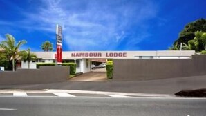 The exterior of Nambour Lodge with a clear sky, palm trees, and a parking area.