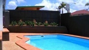 A rectangular swimming pool with a tiled edge, surrounded by a beige textured surface.