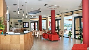 Un moderno vestíbulo de hotel con detalles en rojo, una recepción, zonas de estar y grandes ventanales con vistas.