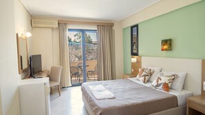 Habitación de hotel con cama, escritorio, silla, televisor y balcón con vistas.