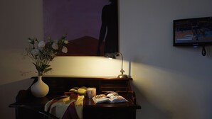 A desk with a book, glasses, a candle, and a vase of flowers. - Venere B&B (Catania)