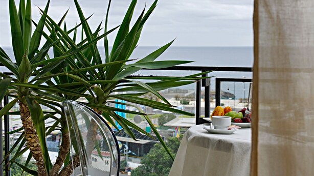 A balcony with a potted plant, a table with a cup and fruit, and a view of the sea. - Venere B&B (Catania)
