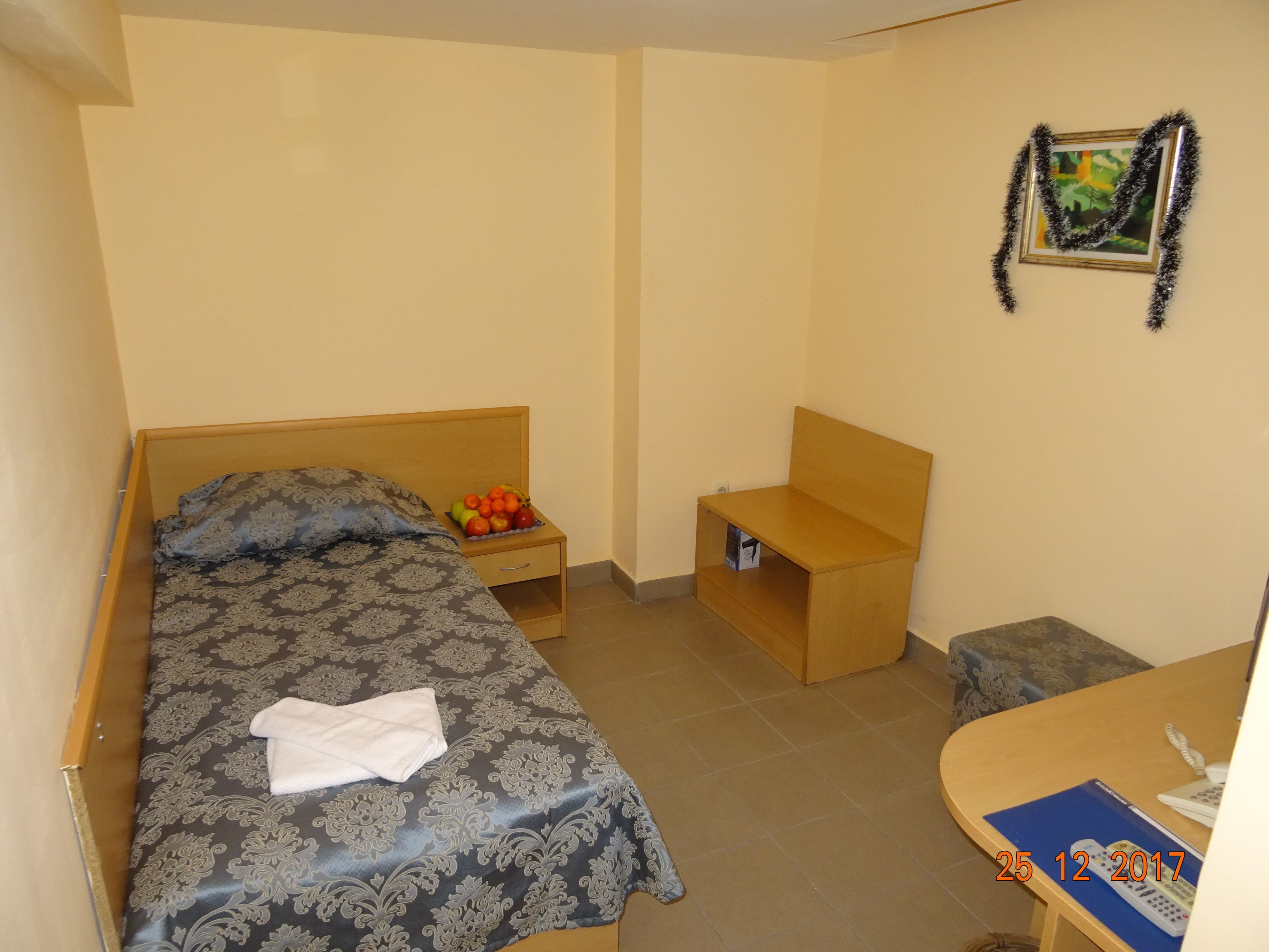 A small, neatly arranged bedroom with a bed, bedside table, and a small desk with a chair.