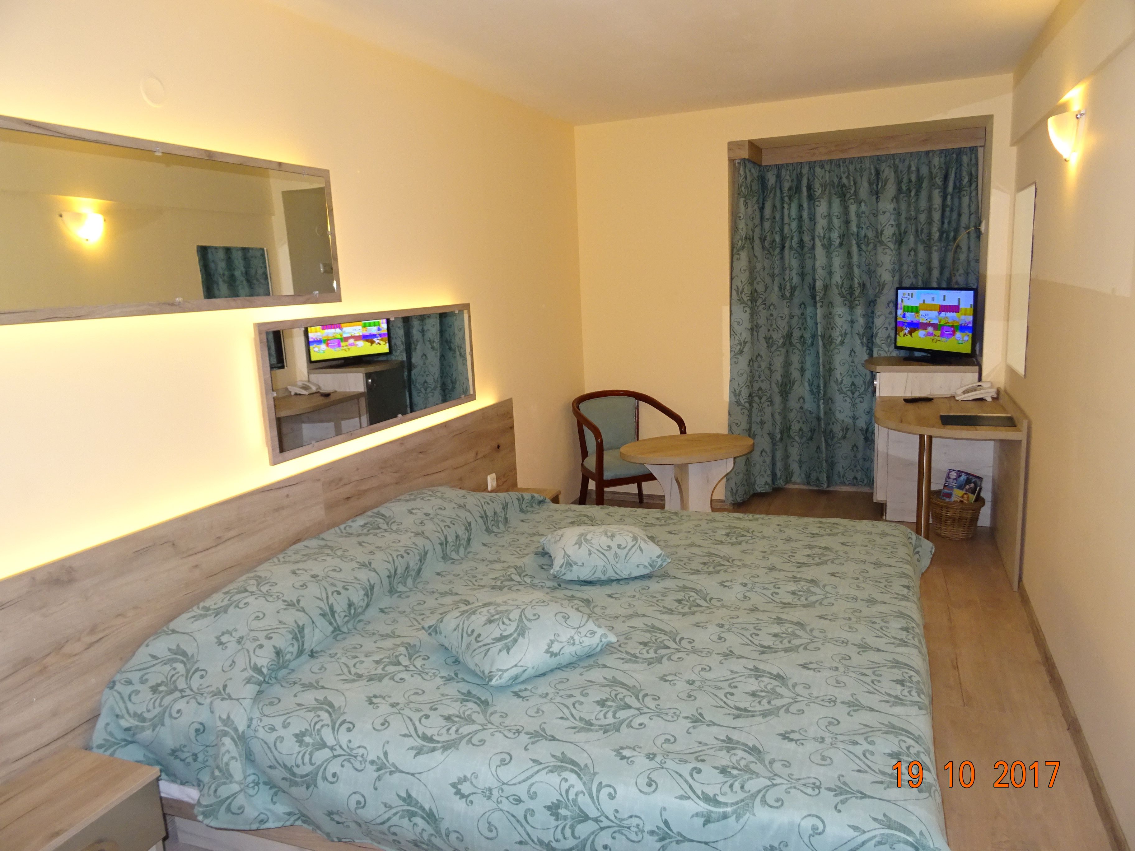 A hotel room with a bed, a desk with a computer, a chair, and a TV.