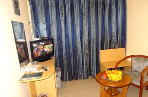 A living room with a TV, a small table with fruit, a chair, and curtains.