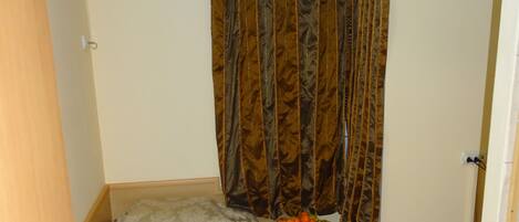Una habitación pequeña con una cama individual, cabecera de madera, mesita de noche con un frutero y una cortina.