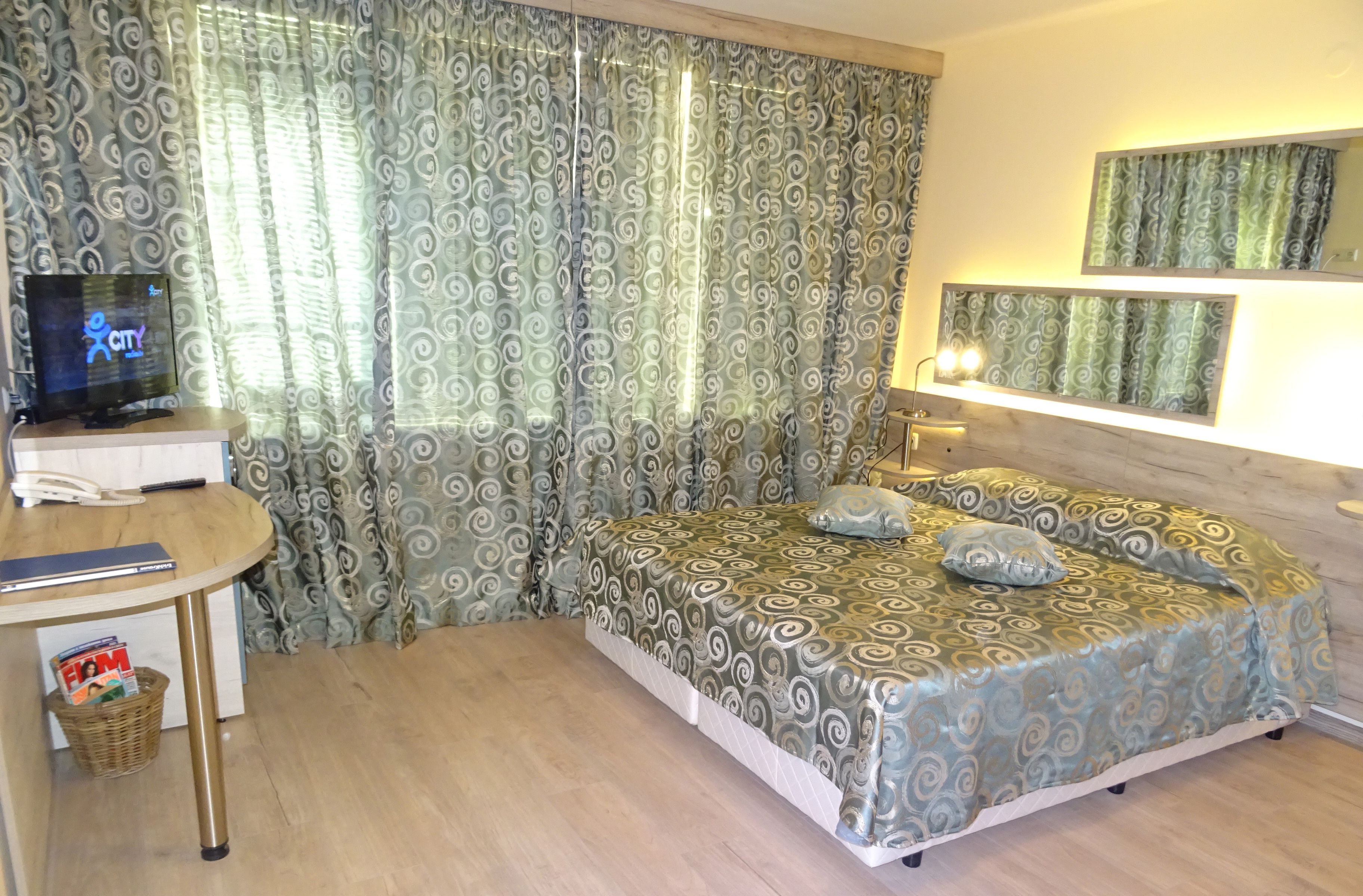 Una habitación de hotel con cama, escritorio, computadora, teléfono y cortinas.