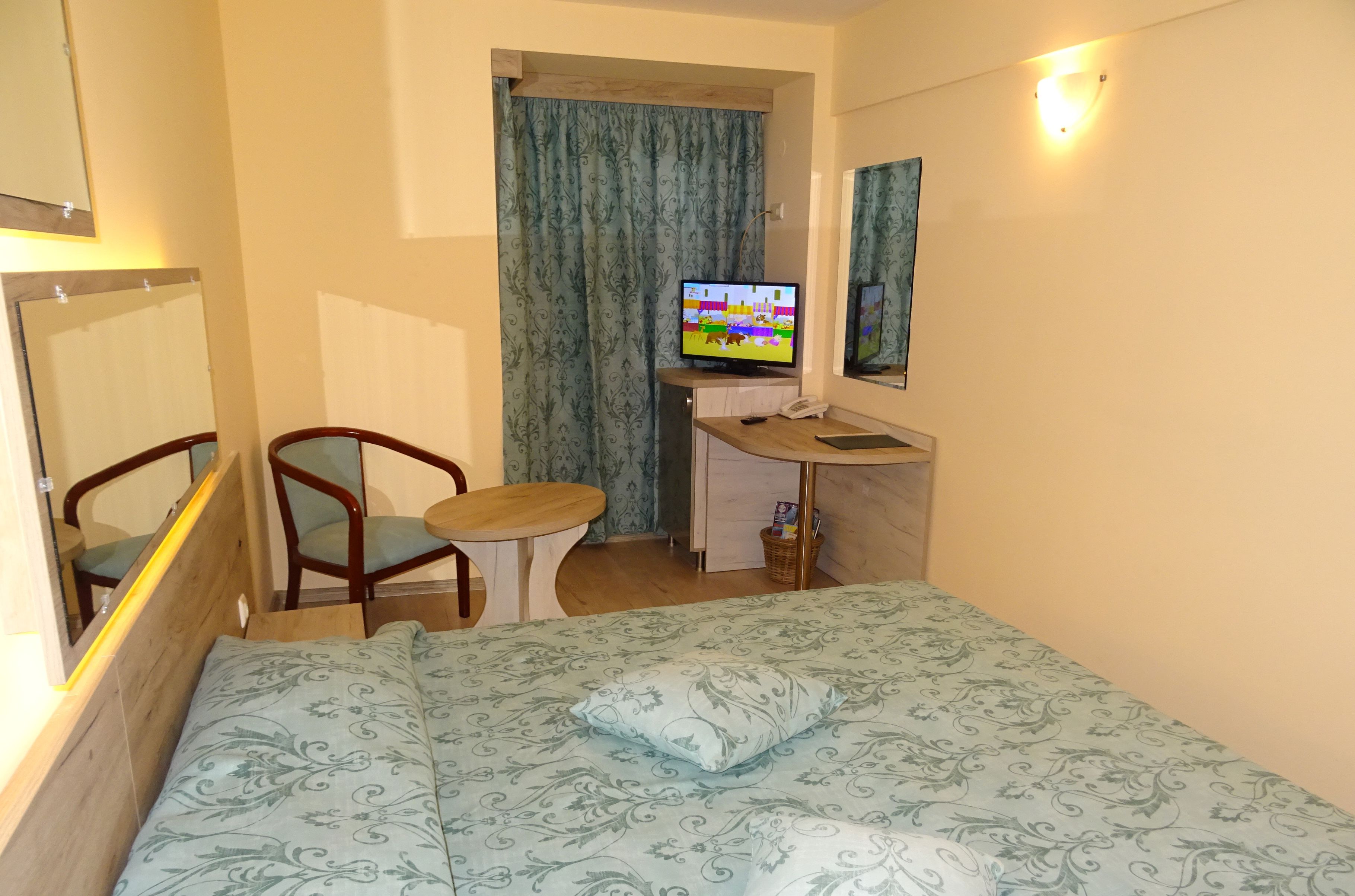 Una habitación de hotel con una cama, un escritorio con computadora, una silla y un televisor.