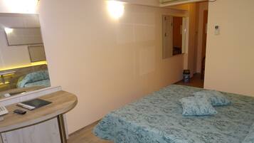 Un dormitorio con cama, escritorio con teléfono y tablet, espejo y puerta que da a otra habitación.