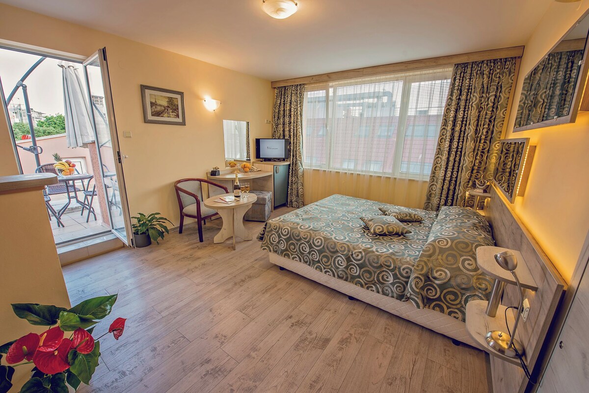 Une chambre à coucher comprenant un lit, un bureau, une chaise, un téléviseur et un balcon avec une table et des chaises.