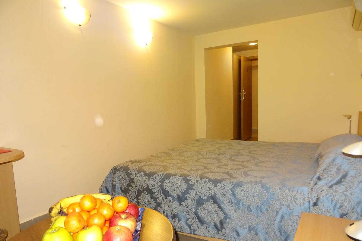 Una habitación de hotel con cama, mesita de noche, lámpara y un frutero en el suelo.