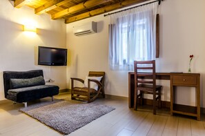 A room with a sofa, a wooden chair, a desk, a TV, and a window with curtains.